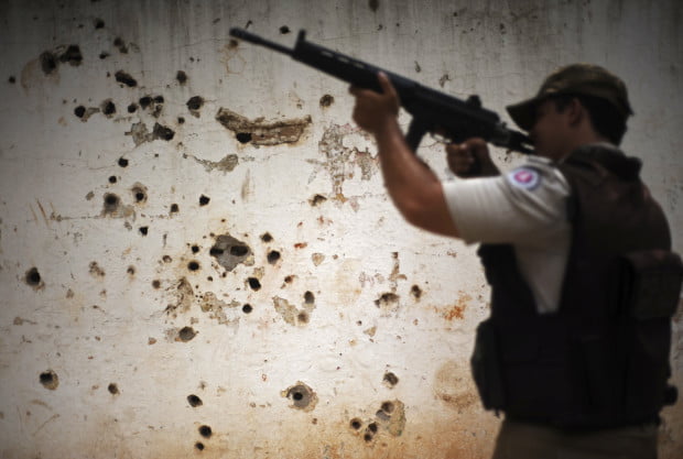 Police patrol past the "rifle wall" pockmarked by bullets in the Nordeste de Amaralina slum complex in Salvador